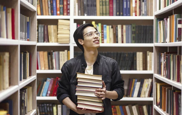 Homem chinês jovem em óculos de pé na biblioteca — Fotografia de Stock