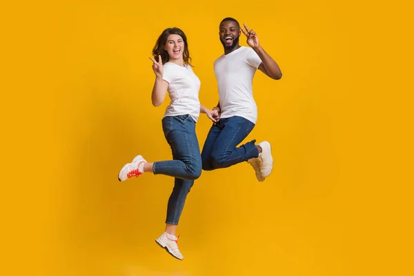 Glückliches Paar trödelt zusammen, springt in die Luft und zeigt Friedenszeichen — Stockfoto