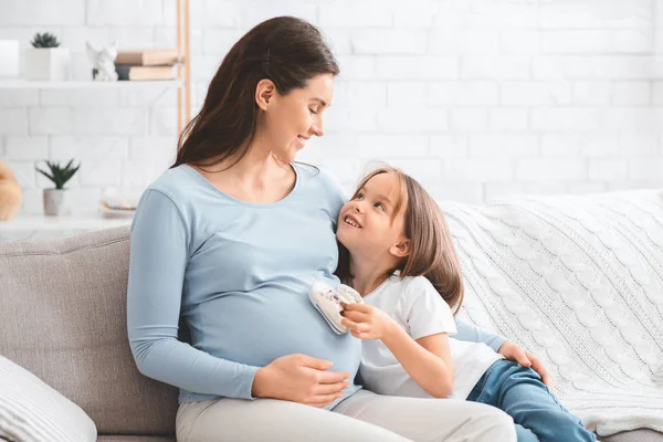 Hijita poniendo pequeñas botas de bebé en la barriga madre embarazada —  Fotos de Stock