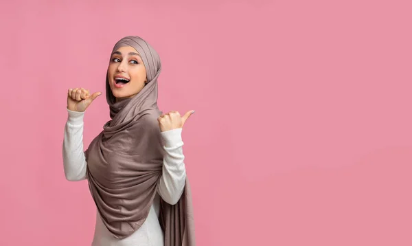 Gioiosa donna musulmana in hijab che indica lo spazio copia dietro di lei — Foto Stock