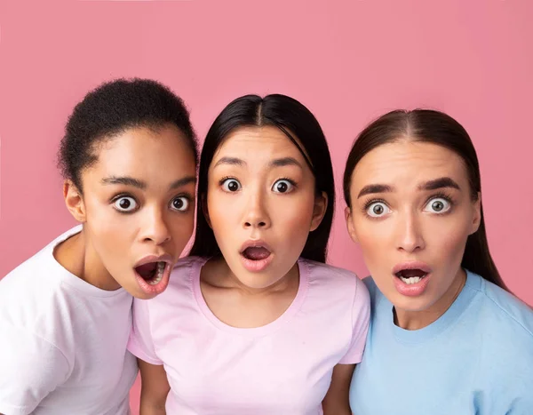 Три удивленные девушки смотрят на камеру, позирующую на розовом фоне — стоковое фото