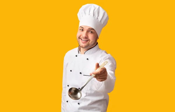 Chef alegre segurando colher concha posando sobre fundo amarelo — Fotografia de Stock