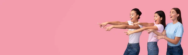 Drie opgewonden meisjes wijzende vingers Afgezien van over roze achtergrond, Panorama — Stockfoto