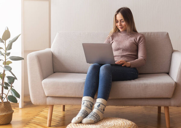 Young girl studying with laptop at home, sitting on couch