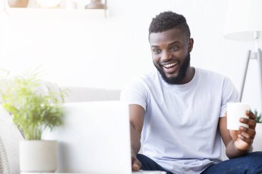 Genç Afrikalı adam laptopta arkadaşlarıyla görüntülü sohbet ediyor.