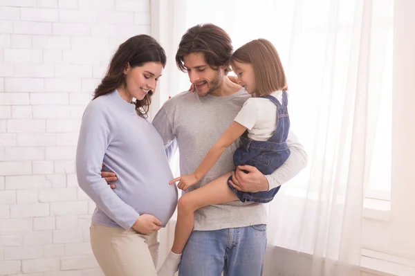 Malá dívka dotýkající se matky těhotné břicho, sblížení s rodiči doma — Stock fotografie