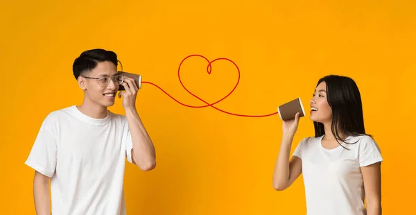 Молодая азиатская пара с баночкой телефон на оранжевом фоне — стоковое фото