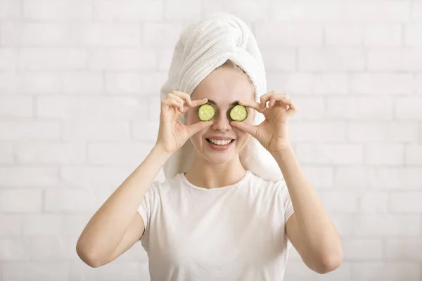 Mujer con toalla en el ojo que cubre la cabeza con rodajas de pepino — Foto de Stock