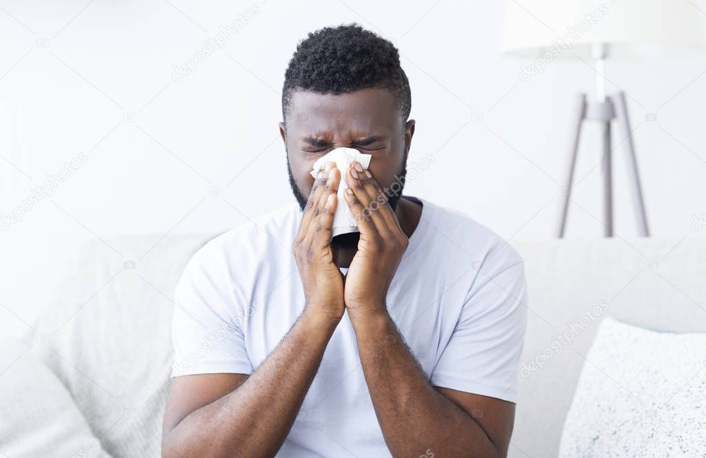Sick african guy cleaning his snotty nose at home