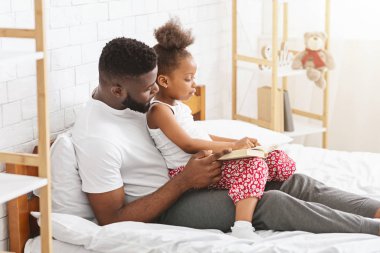 Baba dizinde oturan küçük kız, birlikte kitap okuyor.