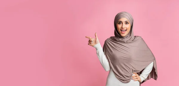 Šťastná islámská žena ukazuje stranou na kopírovací prostor na růžovém pozadí — Stock fotografie