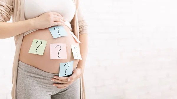 Pregnant woman with question marks on paper stickers on tummy — Stockfoto