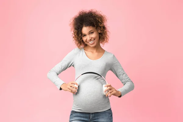 Zwangerschapstherapie. Afro vrouw met koptelefoon op haar buik — Stockfoto