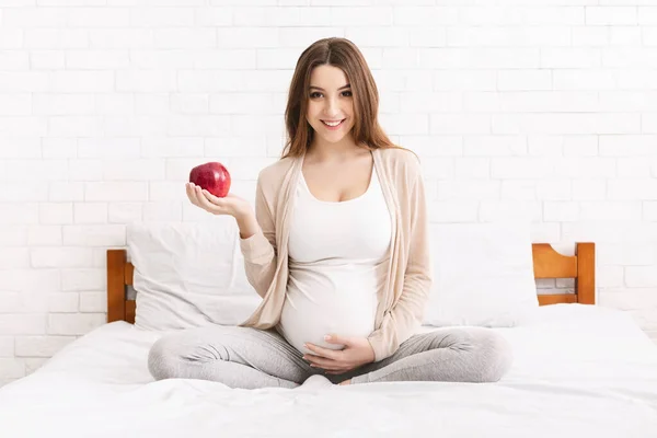 Wanita hamil muda dengan apel merah duduk di tempat tidur — Stok Foto