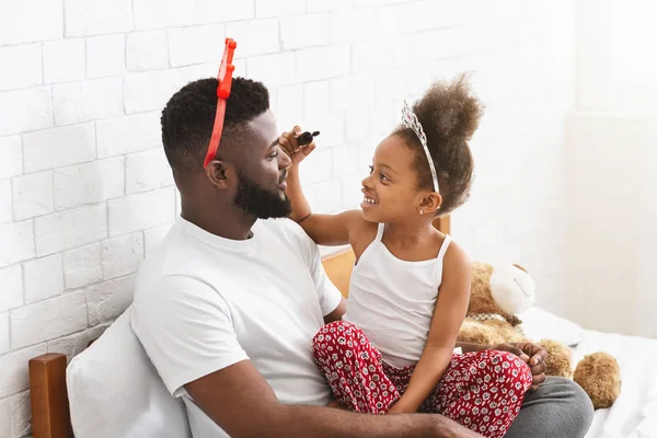 Cute little girl putting mascara on her young dad eyelashes — ストック写真