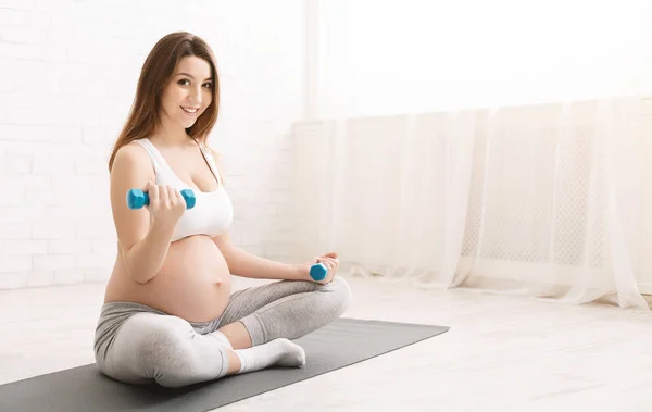 Femme enceinte faisant de l'exercice avec haltères à la maison — Photo