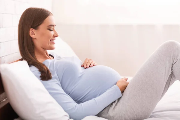 Těhotná dáma dotýkání břicho ležící v posteli, boční pohled — Stock fotografie