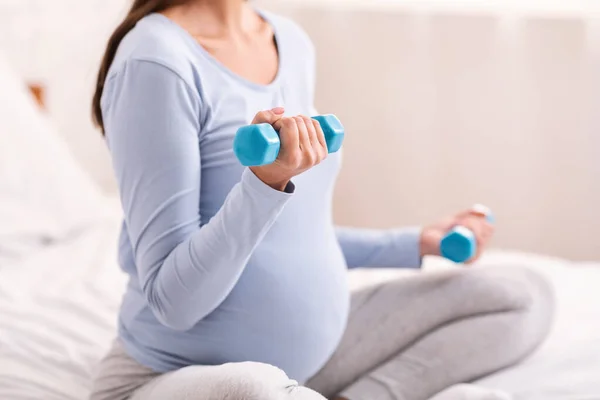 Unrecognizable Expectant Woman Exercising With Dumbbells Sitting On Bed Indoor — Stock Photo, Image