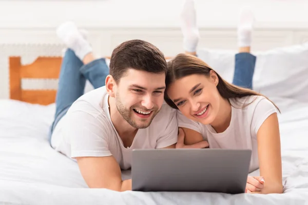 Σύζυγοι που χρησιμοποιούν φορητό υπολογιστή βλέποντας ταινία που βρίσκεται στο κρεβάτι — Φωτογραφία Αρχείου