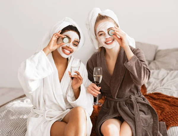 Vrolijke vriendinnen met gezichtsmaskers in badjassen die champagne drinken — Stockfoto