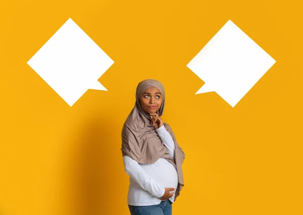 Zamyšlená černošky těhotná žena v hidžábu pózování mezi dvěma řečovými bublinami — Stock fotografie