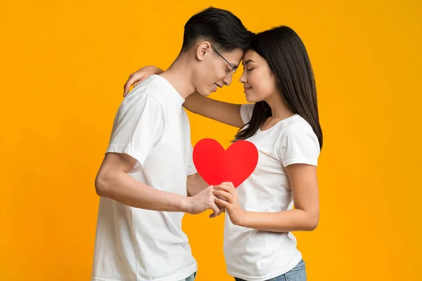 Jovem casal abraçando e segurando coração de amor vermelho — Fotografia de Stock