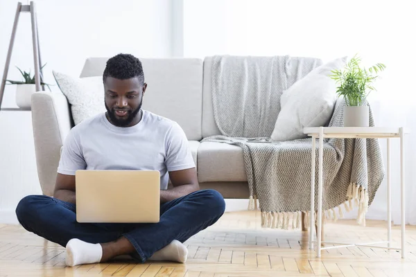 Freelancer preto digitando no laptop, sentado no chão em casa — Fotografia de Stock