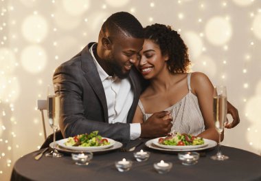 Yakışıklı siyahi adam, şenlikli bir akşam yemeğinde kız arkadaşını kucaklıyor.