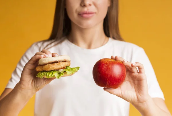 Burger i jabłko w rękach nierozpoznawalnej kobiety, zbliżenie — Zdjęcie stockowe