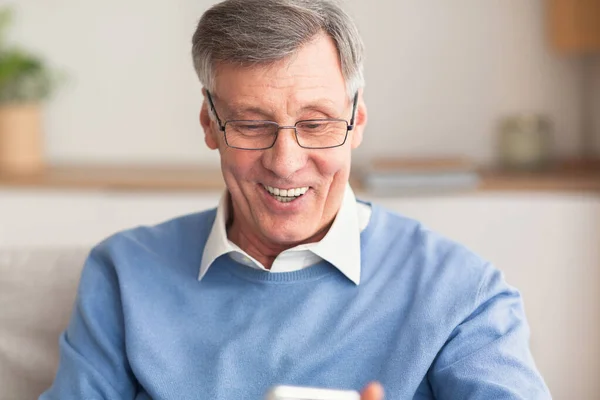 Ηλικιωμένος κύριος κρατώντας κινητό τηλέφωνο ανάγνωση μήνυμα κάθεται στον καναπέ — Φωτογραφία Αρχείου