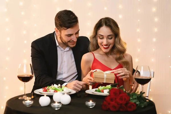 Mujer feliz desenvolviendo regalo de su novio en la fecha en el restaurante — Foto de Stock