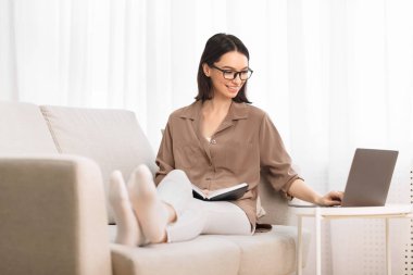 Kanepede oturan ve defter okuyan genç bir kadın.