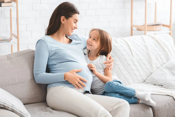 Mujer embarazada alegre hablando con su pequeña hija curiosa — Foto de Stock