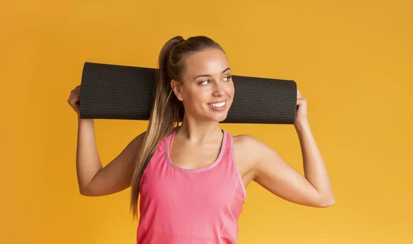 Chica Deportiva sosteniendo estera de yoga en los hombros, sonriendo y mirando hacia otro lado — Foto de Stock