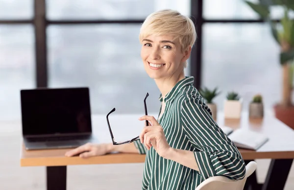Glückliche Geschäftsfrau mittleren Alters sitzt am Schreibtisch im modernen Büro — Stockfoto