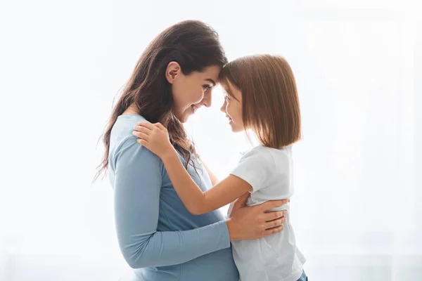 Loving zwangere vrouw knuffelen haar kleine dochter over witte achtergrond — Stockfoto