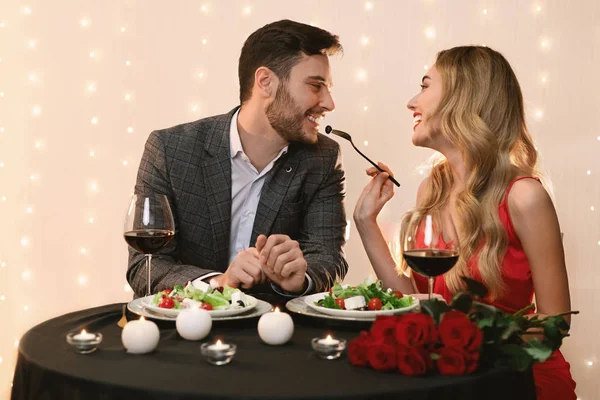 Opiekuńcza kobieta karmiąca chłopaka sałatką na romantycznej randce w restauracji — Zdjęcie stockowe