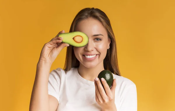 Positive girl holding avocado halves and covering eye with one piece — 스톡 사진