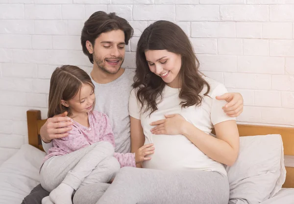 Mujer embarazada, su marido y su hija abrazándose juntos en la cama — Foto de Stock