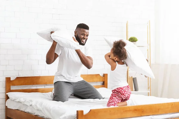 Gülen siyah adam küçük kızıyla yastık savaşı yapıyor. — Stok fotoğraf