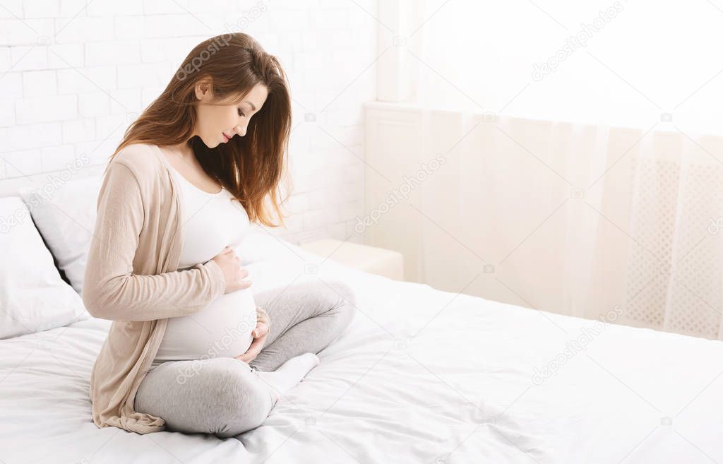 Cheerful expectant woman touching her belly with love