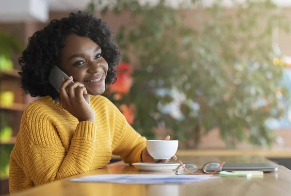 Šťastná mladá černoška pije kávu v kavárně, vede rozhovor — Stock fotografie