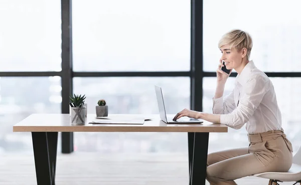 Mujer de negocios hablando por teléfono usando el ordenador portátil en la oficina, Vista lateral — Foto de Stock