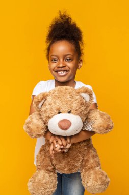 Sarı arka planda oyuncak ayıyı tutan güzel afro kız.