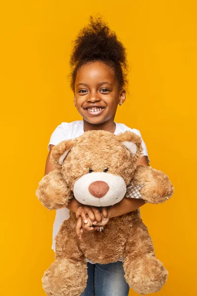 Pretty afro girl holding teddy bear over yellow background — Stock Photo, Image