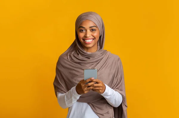 Alegre afro musulmán chica en hiyab con teléfono inteligente en las manos —  Fotos de Stock