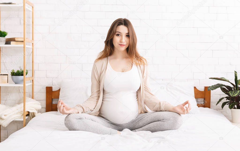 Calm young pregnant woman meditating in bed