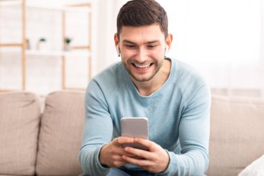 Kulaklıklı Neşeli Adam Smatphone kullanıyor. Kapalı koltukta oturuyor.