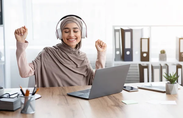 快乐的穆斯林女商人在无线耳机里听音乐，坐在工作场所 — 图库照片