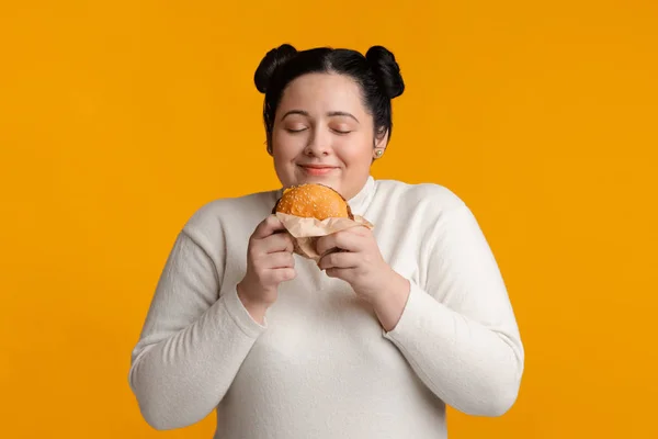 Dagadt Éhes Lány kezében Burger és szagolgatja azt — Stock Fotó